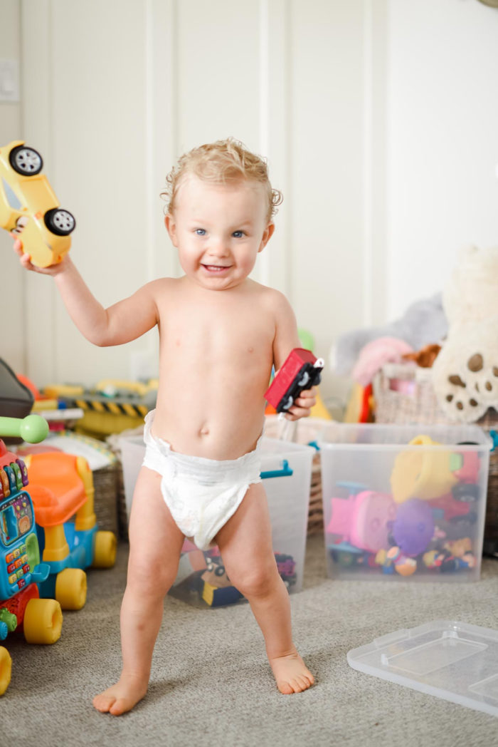 Walmart Baby Registry Must-Have by popular Utah life and style blog, A Slice of Style: image of a little boy wearing only a diaper and holding a yellow toy car in a toy room.