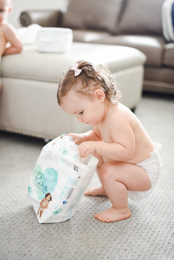 Walmart Baby Registry Must-Have by popular Utah life and style blog, A Slice of Style: image of a little girl wearing only diaper and looking in a package of Pamper's Pure Protection diapers from Walmart