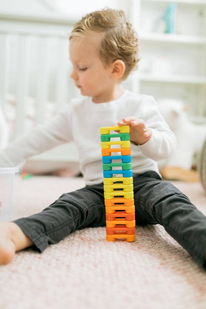 Fun Activities for Kids at Home by popular Utah lifestyle blog, A Slice of Style: image of a little boy sitting on the floor and playing with some stacking toys. 