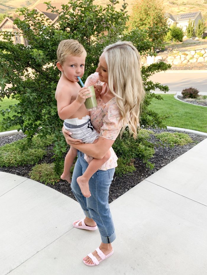 Solgar Vitamins Review + Green Smoothie Recipe by popular Utah life and style blog, A Slice of Style: image of woman standing outside and holding her young son while he drinks a green smoothie.