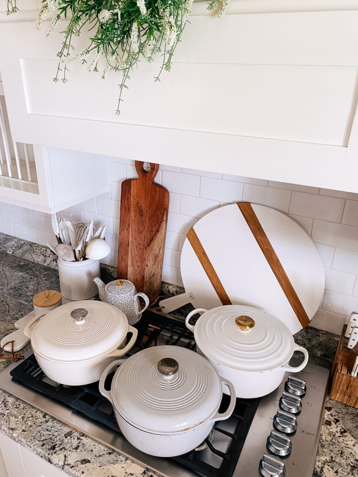 Best Kitchen Tools by popular Utah lifestyle blog, A Slice of Style: image of a farmhouse kitchen with white cabinets, gas range, wood cutting boards, white salter and pepper shakers, and white dutch ovens. 