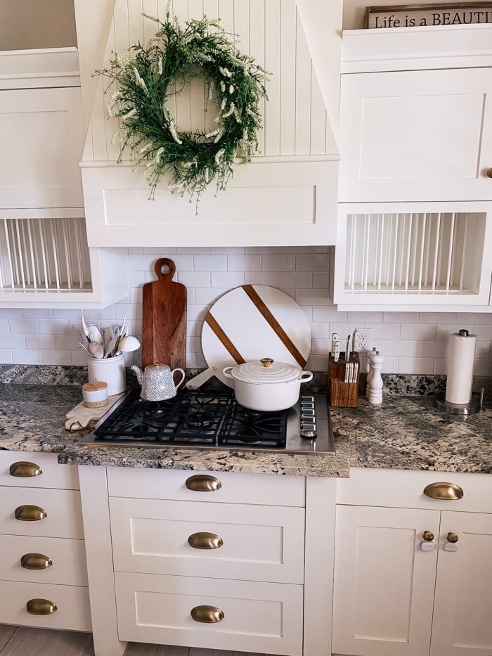 Best Kitchen Tools by popular Utah lifestyle blog, A Slice of Style: image of a farmhouse kitchen with white cabinets, gas range, wood cutting boards, white salter and pepper shakers, and a white dutch oven. 