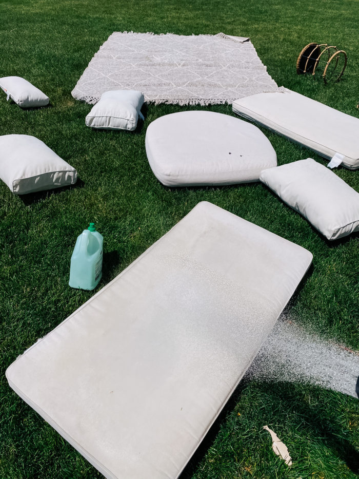 White Outdoor Cushions by popular Utah life and style blog, A Slice of Style: image of a white outdoor cushions and a grey and white outdoor rug spread out on the grass and being sprayed down with a hose. 