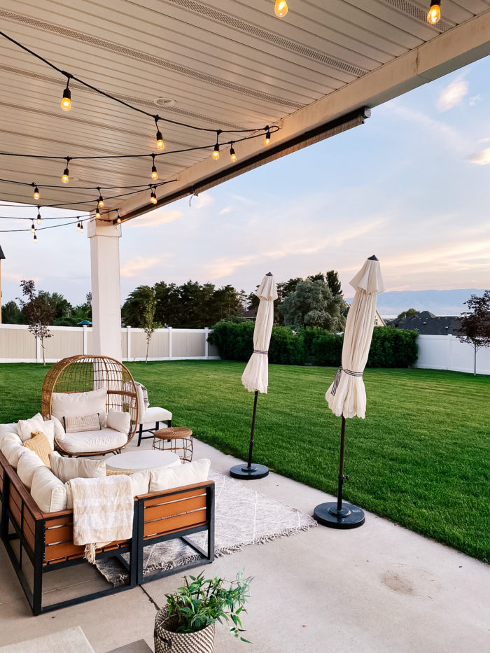 White Outdoor Cushions by popular Utah life and style blog, A Slice of Style: image of a backyard patio with bistro lights, white shade umbrellas, patio furniture and white outdoor cushions. 