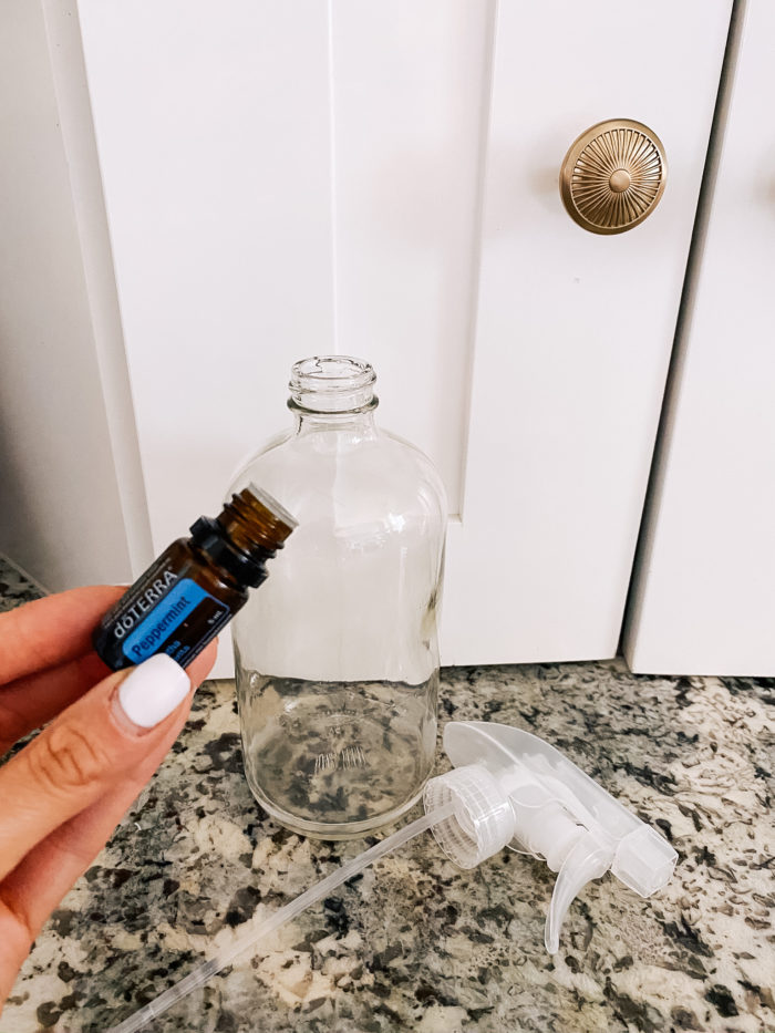 White Outdoor Cushions by popular Utah life and style blog, A Slice of Style: image of Jenica Parcell holding a bottle of doTERRA peppermint oil next to a glass spray bottle.