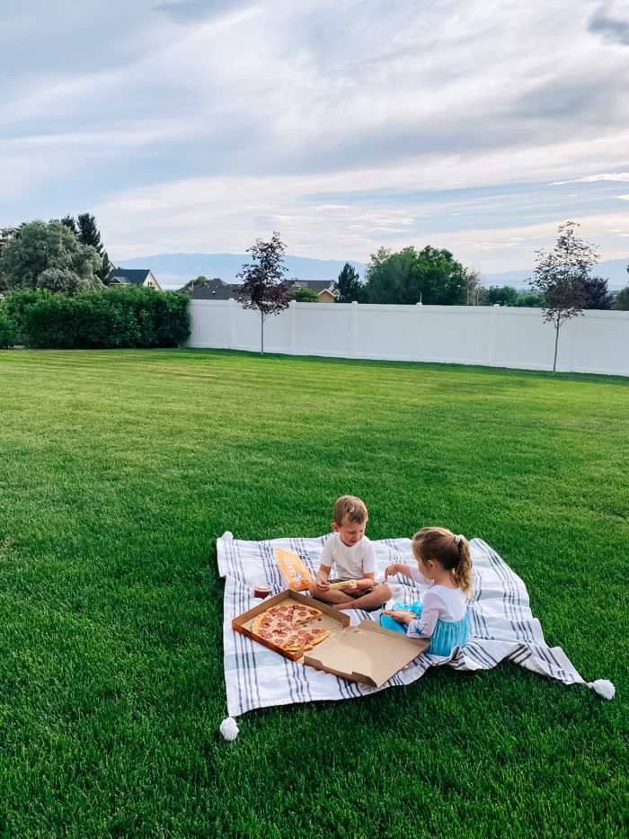 White Outdoor Cushions by popular Utah life and style blog, A Slice of Style: image of two kids eating pizza and sitting on a white and grey stripe blanket in their backyard.