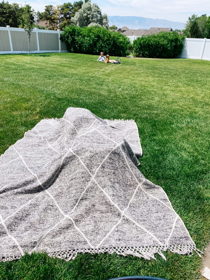 White Outdoor Cushions by popular Utah life and style blog, A Slice of Style: image of a wet grey and white outdoor rug drying on the grass.