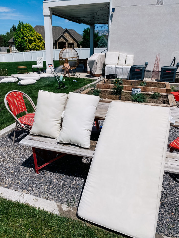 White Outdoor Cushions by popular Utah life and style blog, A Slice of Style: image of a white outdoor cushions and a grey and white outdoor rug spread out on the grass and propped up on a picnic table to dry. 