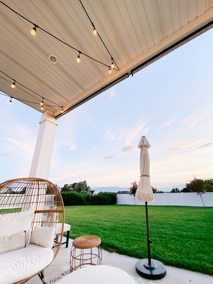 White Outdoor Cushions by popular Utah life and style blog, A Slice of Style: image of a backyard patio with bistro lights, white shade umbrellas, patio furniture and white outdoor cushions. 