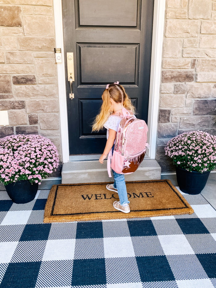 Back to School Checklist by popular Utah motherhood blog, A Slice of Style: image of a young girl wearing a Walmart Wonder Nation Baby Girls & Toddler Girls Heart Knee Patch Jeans, Walmart Wonder Nation Casual Bump Toe Sneaker, Limited Too Girl's Metallic & Glitter Backpack with Lunch Bag and standing on her front porch steps. 